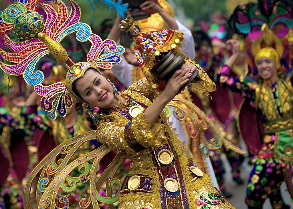 A picture from the Sinulog Festival of a woman dancing, adorned in costume, with a religious statue in her hands.